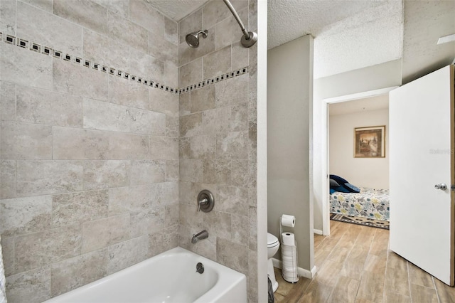 bathroom with a textured ceiling, wood-type flooring, tiled shower / bath combo, and toilet