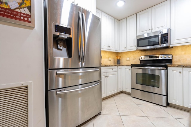 kitchen with appliances with stainless steel finishes, light tile patterned floors, white cabinetry, and dark stone counters