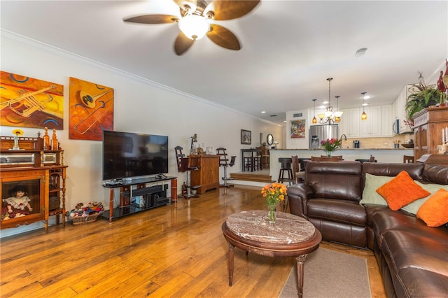 living room featuring ceiling fan with notable chandelier, ornamental molding, and light hardwood / wood-style flooring