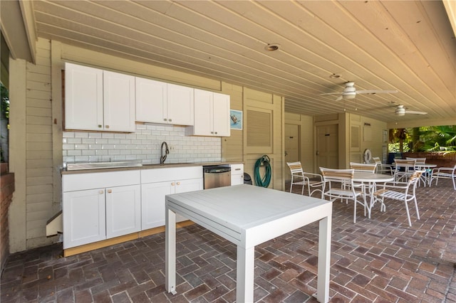 kitchen featuring decorative backsplash, stainless steel dishwasher, ceiling fan, white cabinets, and wood walls