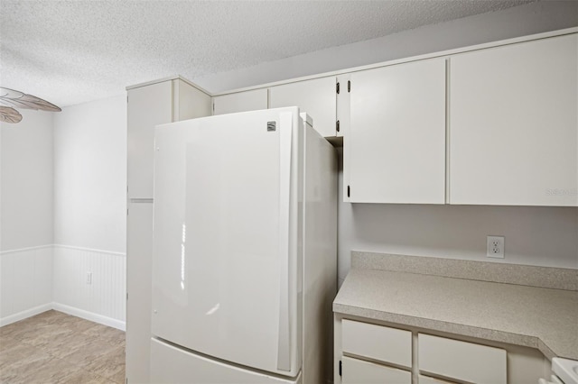 kitchen with white refrigerator, white cabinets, and a textured ceiling