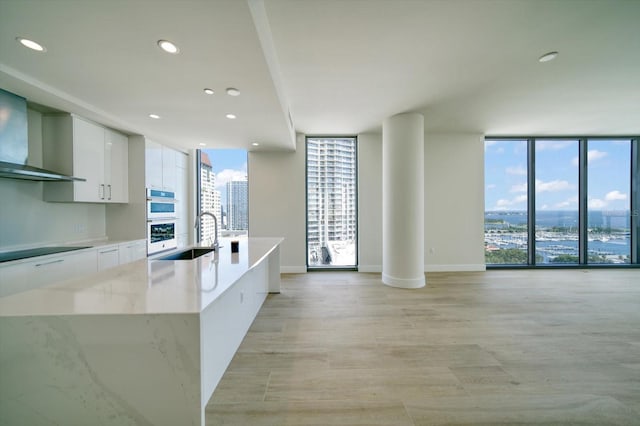 kitchen with sink, white cabinetry, a center island with sink, double oven, and expansive windows