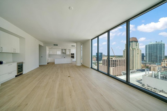 unfurnished living room featuring expansive windows, wine cooler, and light hardwood / wood-style floors