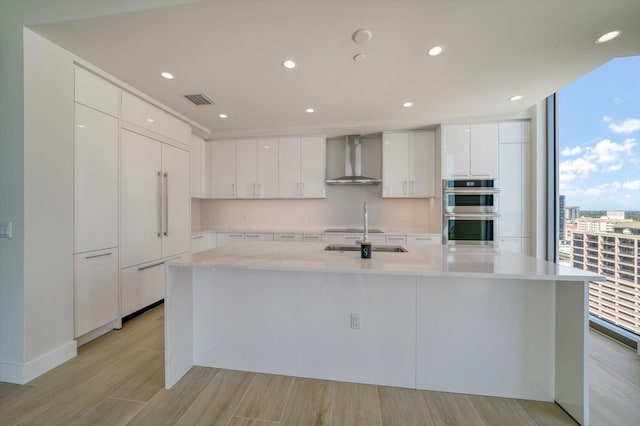 kitchen featuring stainless steel double oven, plenty of natural light, wall chimney range hood, and white cabinetry