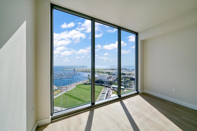 spare room with wood-type flooring, a water view, plenty of natural light, and floor to ceiling windows