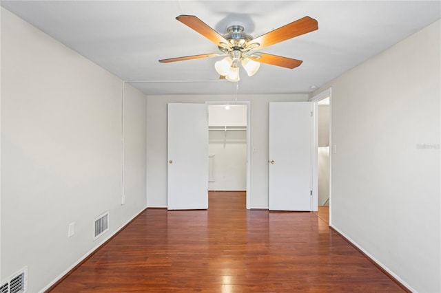 unfurnished bedroom with ceiling fan, a walk in closet, dark hardwood / wood-style flooring, and a closet