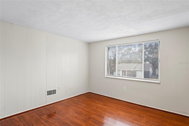 spare room featuring wood walls, hardwood / wood-style floors, and a textured ceiling