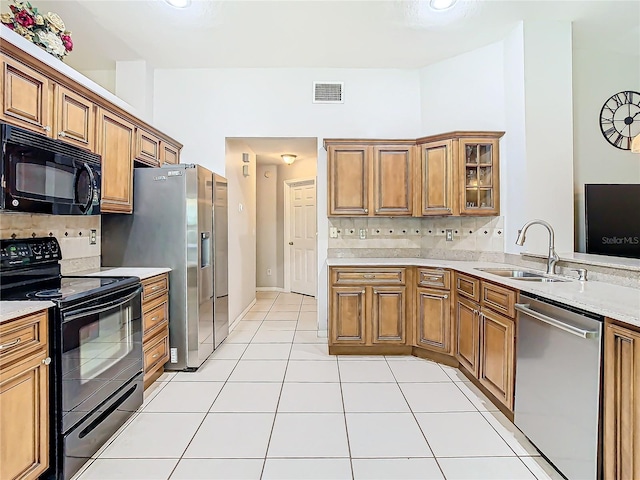 kitchen with tasteful backsplash, light stone countertops, light tile patterned floors, black appliances, and sink