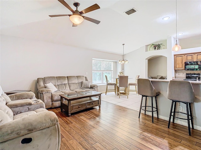 living room with ceiling fan with notable chandelier, light wood-type flooring, and lofted ceiling