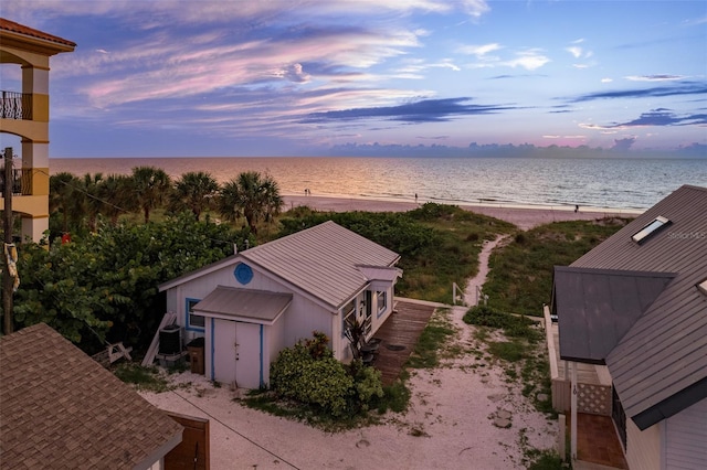 aerial view at dusk featuring a water view and a view of the beach