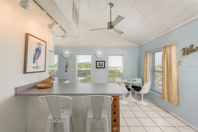 interior space with wood ceiling, vaulted ceiling, kitchen peninsula, light tile patterned floors, and ceiling fan