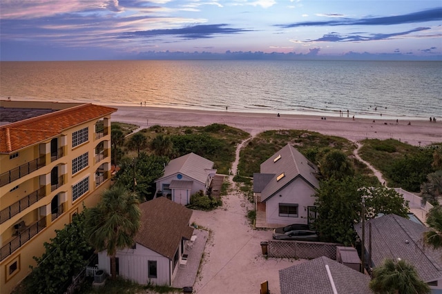 aerial view at dusk featuring a view of the beach and a water view