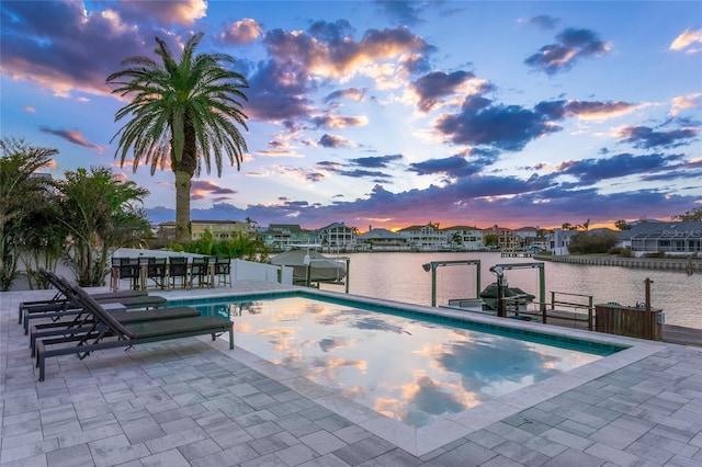 pool at dusk featuring a water view, a patio, and a dock