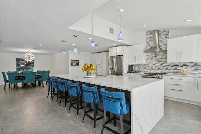 kitchen featuring a large island, white cabinetry, appliances with stainless steel finishes, wall chimney range hood, and pendant lighting