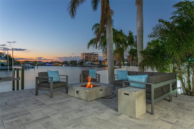 patio terrace at dusk with a dock, a water view, and an outdoor fire pit