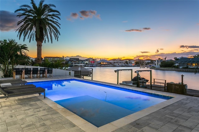 pool at dusk with a patio and a water view