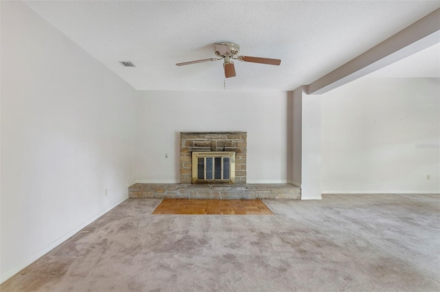 unfurnished living room with ceiling fan, a stone fireplace, a textured ceiling, and light colored carpet