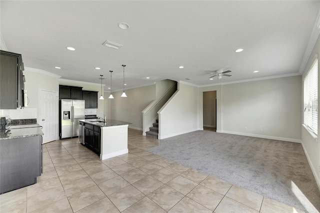 kitchen with a kitchen island with sink, light colored carpet, appliances with stainless steel finishes, crown molding, and ceiling fan