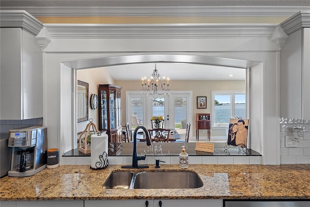 kitchen featuring a water view, sink, decorative backsplash, a notable chandelier, and light stone counters