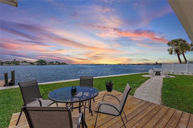 deck at dusk with a water view and a lawn