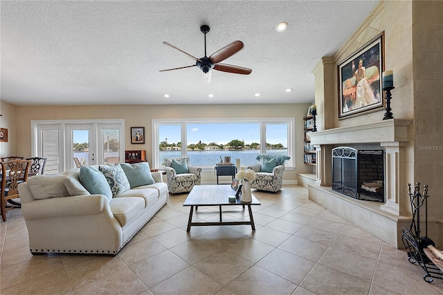 tiled living room with plenty of natural light, a water view, a textured ceiling, and a high end fireplace