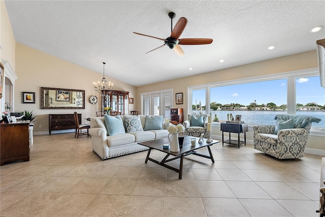 tiled living room featuring ceiling fan with notable chandelier, a water view, lofted ceiling, and a textured ceiling