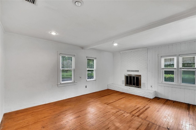 unfurnished living room featuring wood-type flooring, beamed ceiling, a fireplace, and ornamental molding