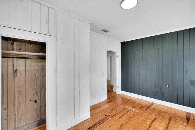 unfurnished bedroom with ornamental molding, a closet, wood walls, and light hardwood / wood-style floors