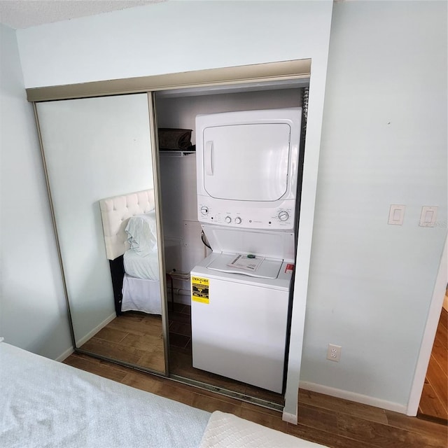 laundry room with stacked washer / drying machine and dark hardwood / wood-style flooring