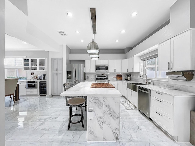 kitchen featuring a center island, white cabinets, sink, appliances with stainless steel finishes, and decorative light fixtures