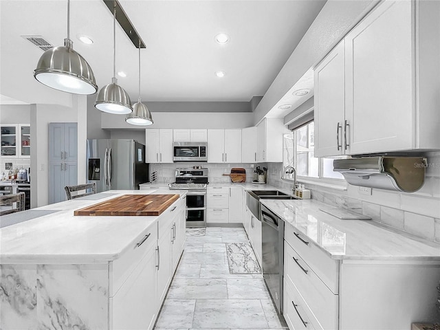 kitchen with decorative backsplash, appliances with stainless steel finishes, light stone counters, pendant lighting, and white cabinetry