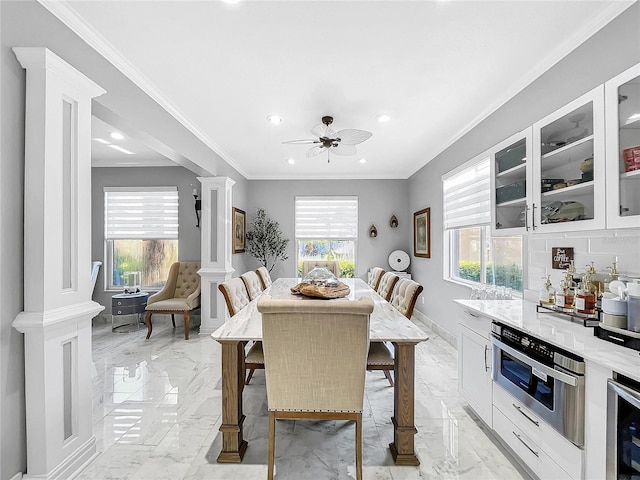 dining area with ornate columns, ceiling fan, a wealth of natural light, wine cooler, and crown molding