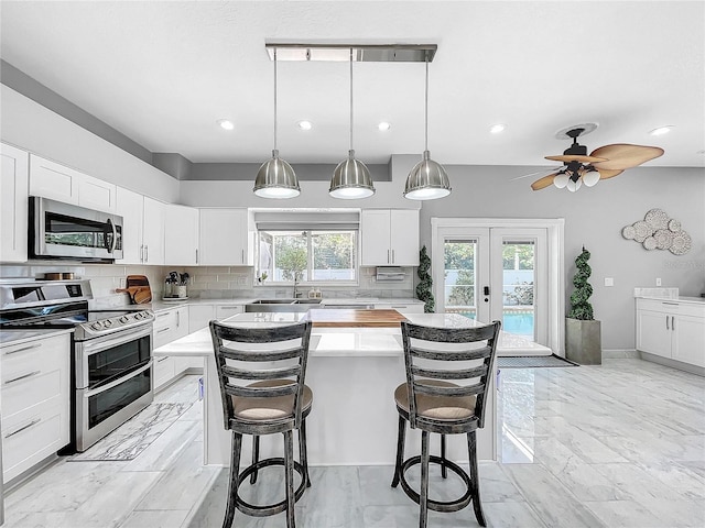 kitchen featuring tasteful backsplash, white cabinetry, a kitchen island, and appliances with stainless steel finishes