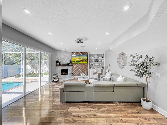 living room featuring built in shelves, a stone fireplace, a textured ceiling, and hardwood / wood-style flooring