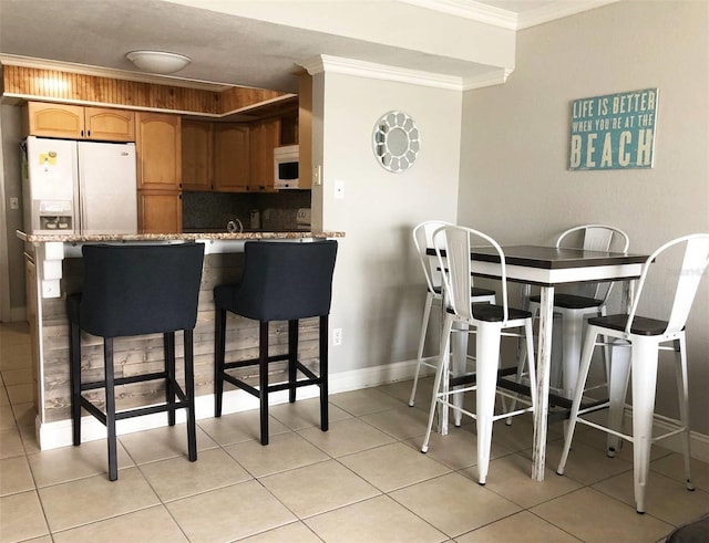 kitchen with a breakfast bar, white appliances, kitchen peninsula, light tile patterned floors, and ornamental molding