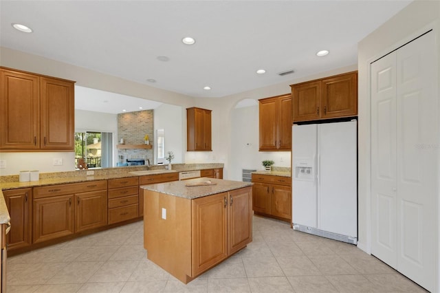 kitchen with white refrigerator with ice dispenser, a center island, kitchen peninsula, light stone counters, and sink