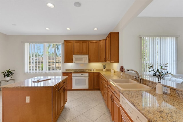 kitchen with white appliances, kitchen peninsula, light stone counters, and sink