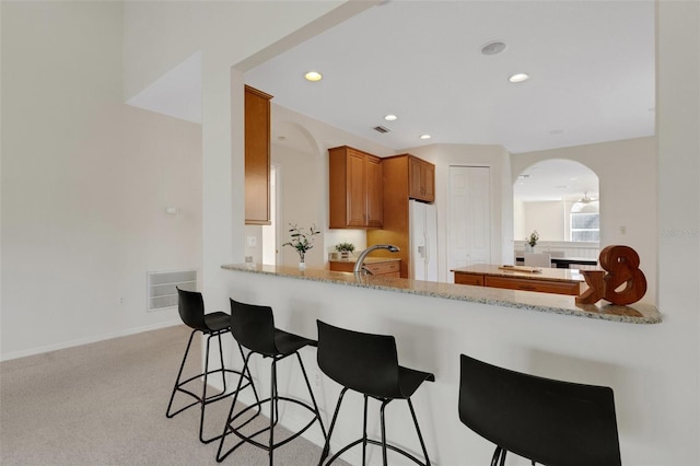 kitchen featuring sink, kitchen peninsula, light stone countertops, white refrigerator with ice dispenser, and light colored carpet