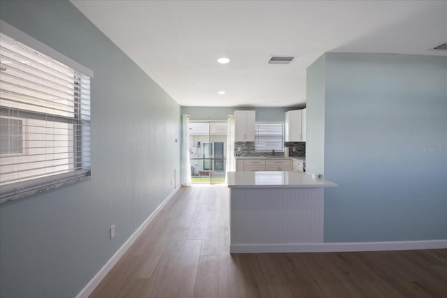 kitchen with white cabinets, sink, kitchen peninsula, backsplash, and light wood-type flooring