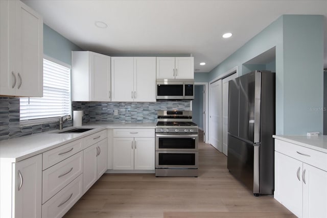 kitchen with sink, white cabinets, light hardwood / wood-style flooring, backsplash, and appliances with stainless steel finishes