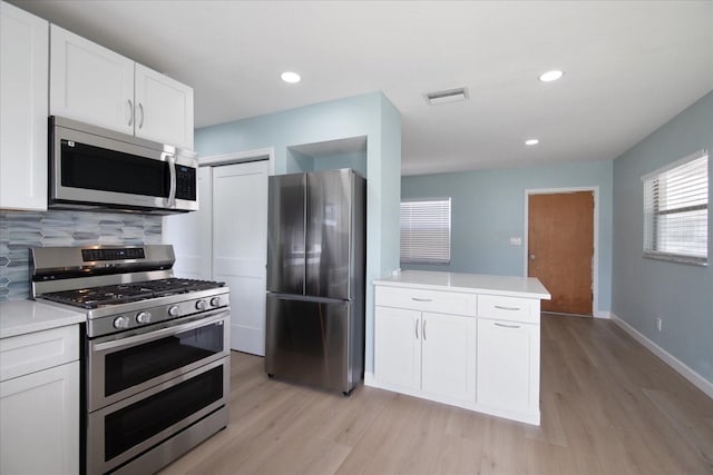 kitchen with stainless steel appliances, white cabinets, light hardwood / wood-style floors, and backsplash