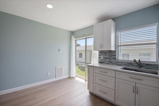 kitchen with light hardwood / wood-style flooring, white cabinetry, tasteful backsplash, and sink