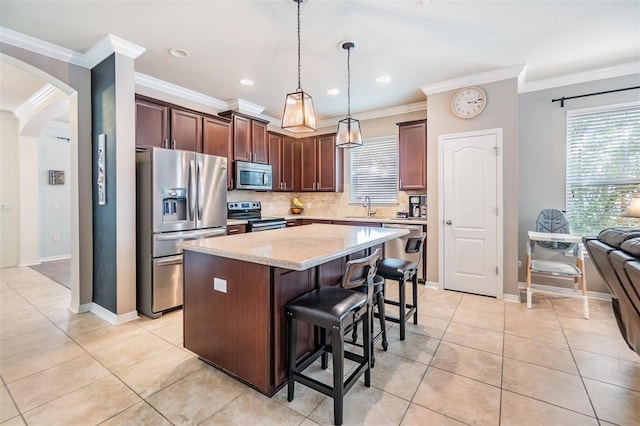 kitchen with appliances with stainless steel finishes, ornamental molding, sink, pendant lighting, and a kitchen island