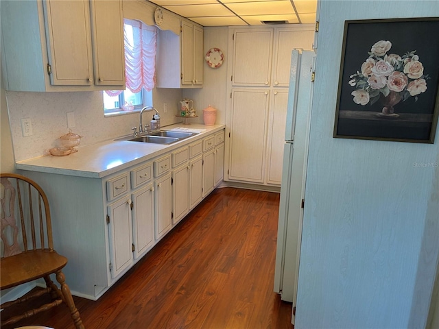 kitchen featuring white cabinetry, white fridge, a drop ceiling, dark hardwood / wood-style floors, and sink