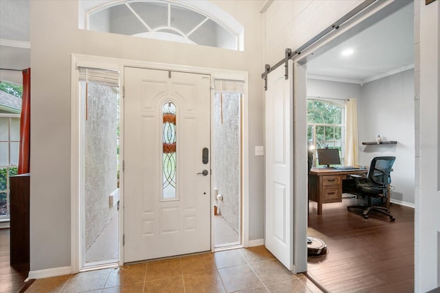 entrance foyer with a barn door, ornamental molding, and light hardwood / wood-style flooring