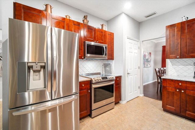 kitchen featuring light stone counters, light tile patterned floors, appliances with stainless steel finishes, and tasteful backsplash