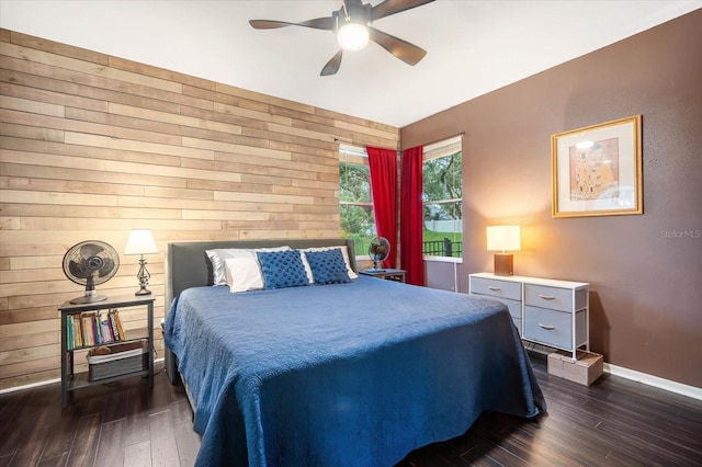 bedroom featuring ceiling fan, wooden walls, and dark wood-type flooring