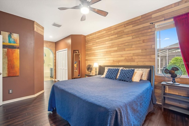 bedroom with a closet, wooden walls, ceiling fan, and dark wood-type flooring