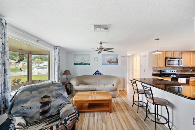 living room with a textured ceiling, light hardwood / wood-style floors, and ceiling fan