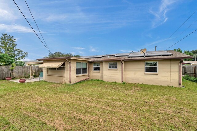 rear view of property with solar panels and a yard